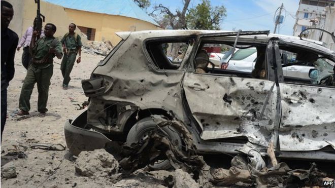 Сомалийские правительственные солдаты идут вокруг разрушенной машины на месте взрыва автомобильной бомбы перед гостиницей Мекка Аль Мукаррама в Могадишо 15 марта 2014 года.