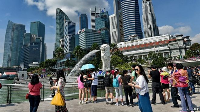 Туристы посещают знаменитый сингапурский Merlion (C) перед горизонтом финансового делового района города 25 февраля 2015 года.