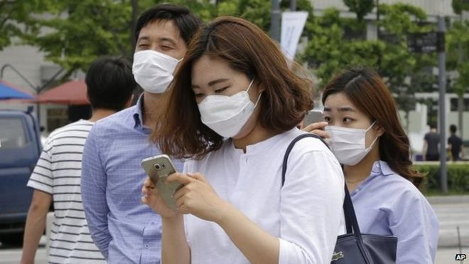 Женщина носит маску в качестве меры предосторожности против вируса ближневосточного респираторного синдрома (MERS), когда она использует свой смартфон на улице в Сеуле, Южная Корея, во вторник, 2 июня 2015 года.