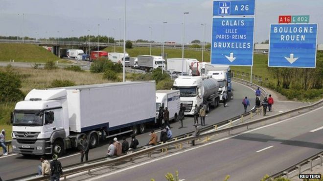 Более десятка мигрантов собираются возле грузовиков, которые ждут на дороге, ведущей к туннелю Ла-Манша, в надежде сесть на них, чтобы совершить тайный переход в Англию