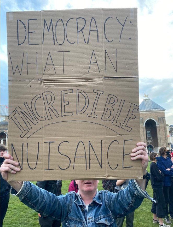 A man holds a placard that reads: "Democracy what an incredible nuisance"
