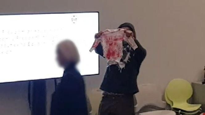 A protester at the front of the lecture hall holding baby clothing covered in fake blood