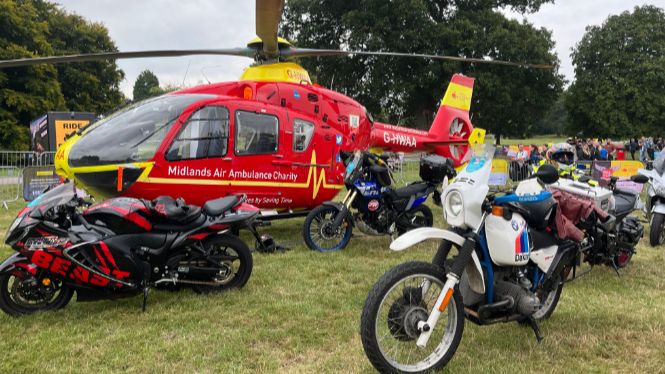 An air ambulance helicopter is stationary in a field with motorbikes parked around it