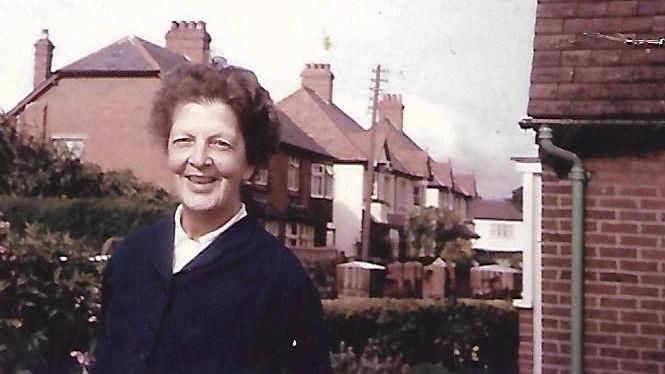 An old photo of an older woman smiling outside a house