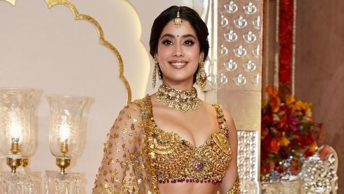 Actress Janhvi Kapoor dressed in a golden wedding outfit smiles at the camera. 