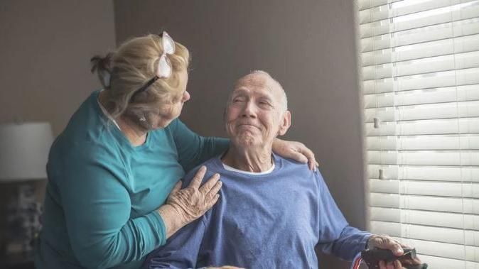 A woman putting her arms around her husband in a wheelchair