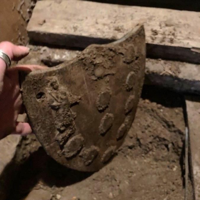 A hand holding an ancient piece broken of pottery with small circles on it.