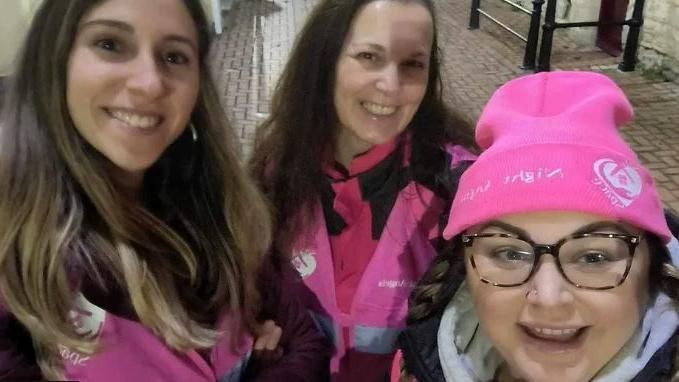 Three Night Angels volunteers in pink hi vis clothing and hats smiling
