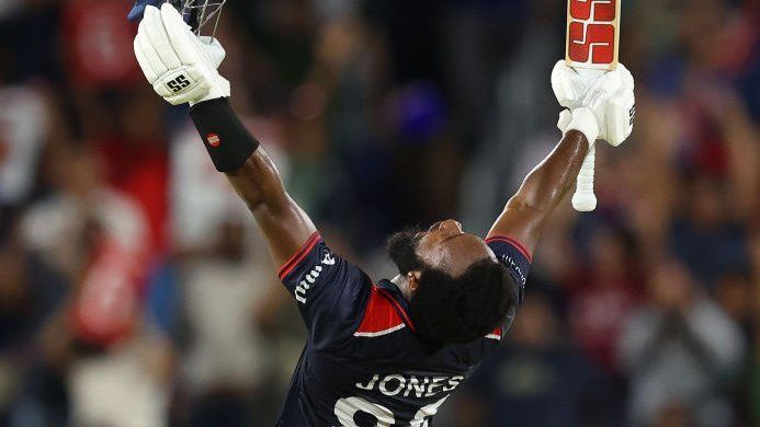 USA batter Aaron Jones kneels and raises hit bat and helmet in celebration