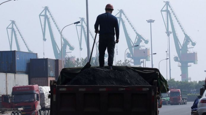 A labourer loads coal in a truck next to containers outside a logistics center near Tianjin Port, in northern China, 16 May, 2019.