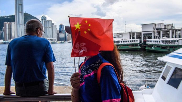 A woman holds Chinese and Hong Kong flags as she gets off a boat in Victoria Harbour on 1 July 2020