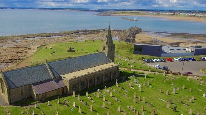 An aerial view of St Bartholomew Church in Newbiggin with the Maritime Centre behind and the sea in the background.