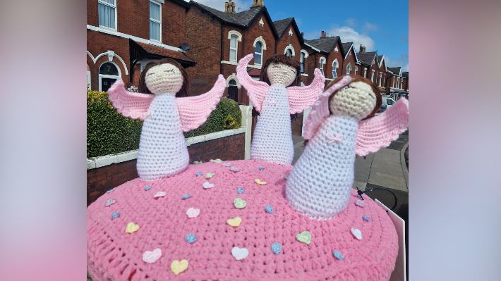 A knitted design of three angels sits on top of a post box