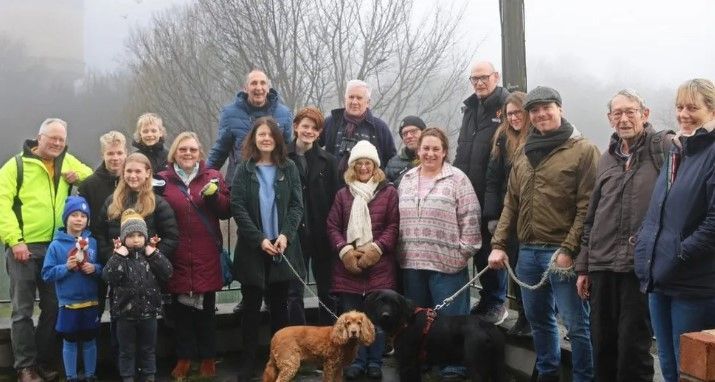 A group of people and two dogs are pictured on the site with the water tower in the faint, misty distance 