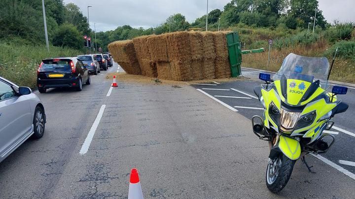 A lorry carrying bales lies on its side across a road. 