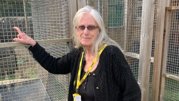 Judy Knowles, with white hair and a yellow lanyard standing outside a large animal cage