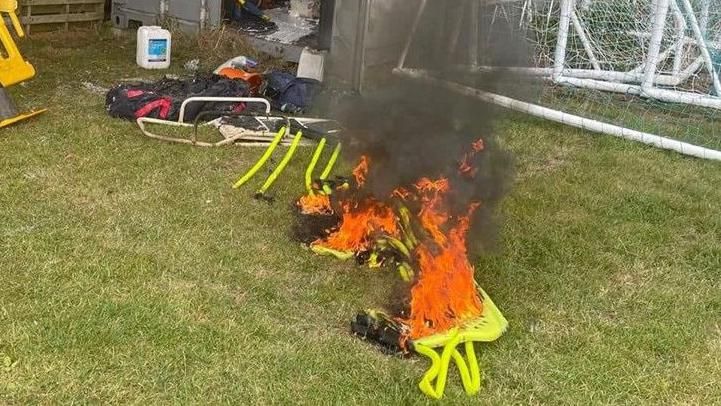 Lime green football apparatus is seen up in flames on the grass at Webbswood Stadium.