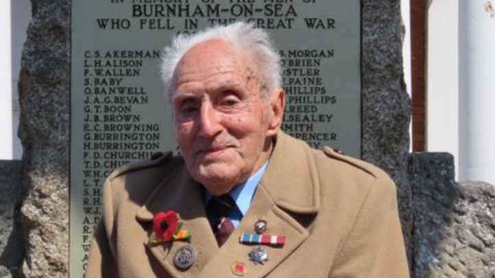 An elderly man wearing a brown coat with medals and a poppy on