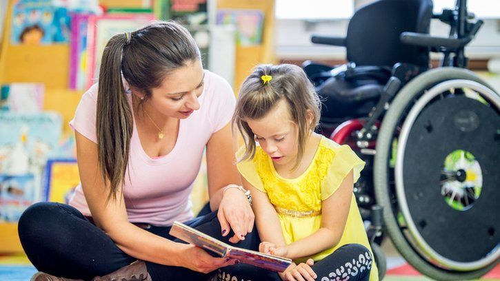 child reading with a teacher with a wheelchair in the background
