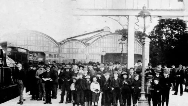 A black and white photograph of crowds of people next to a steam train at Alnwick station 
