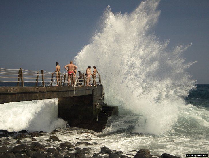 Holidaymakers near a large wave