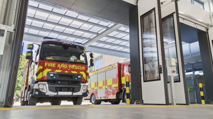 Fire engines in the garage of the new site, the garage doors lifted overhead.