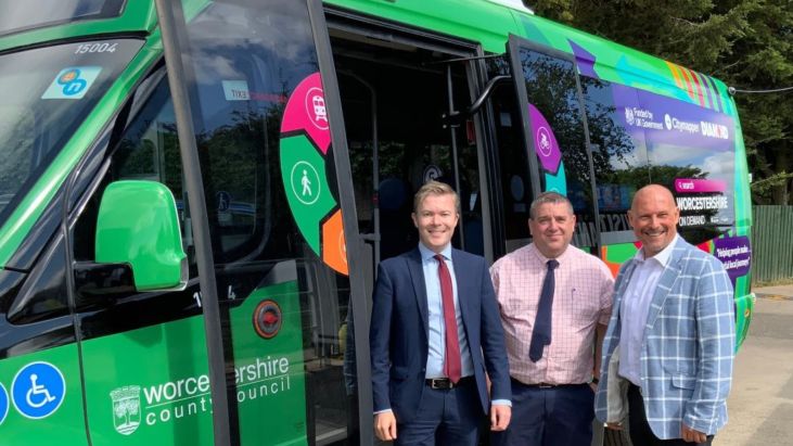 Three men standing in front of a green minibus. They are wearing ties and jackets.