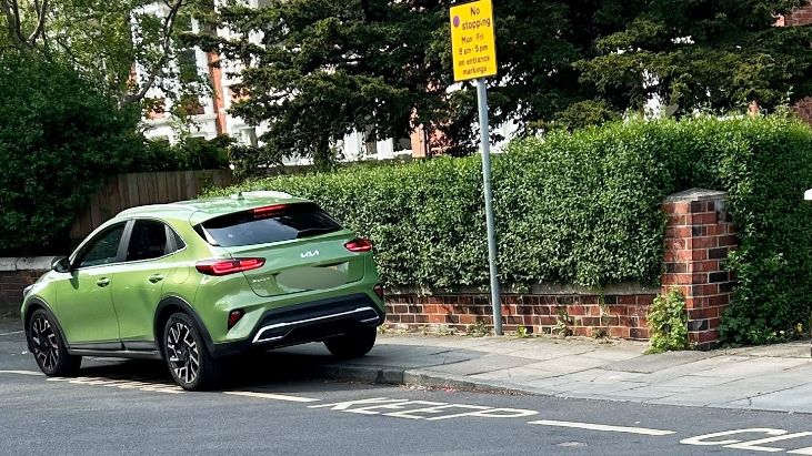 Green car parked over road markings saying 'school keep clear'