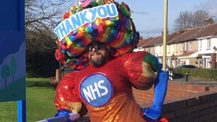 Colin wearing a huge dress with NHS on it - and a headdress which says Thank you