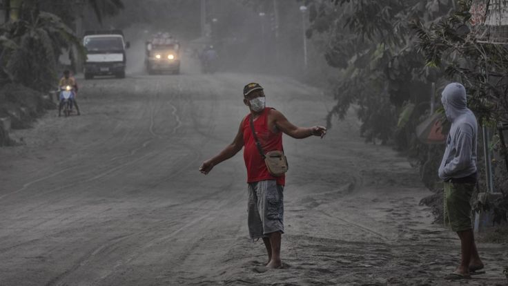 Residents walk along a road covered in volcanic ash from Taal Volcano's eruption on January 13, 2020 in Lemery, Batangas province, Philippines