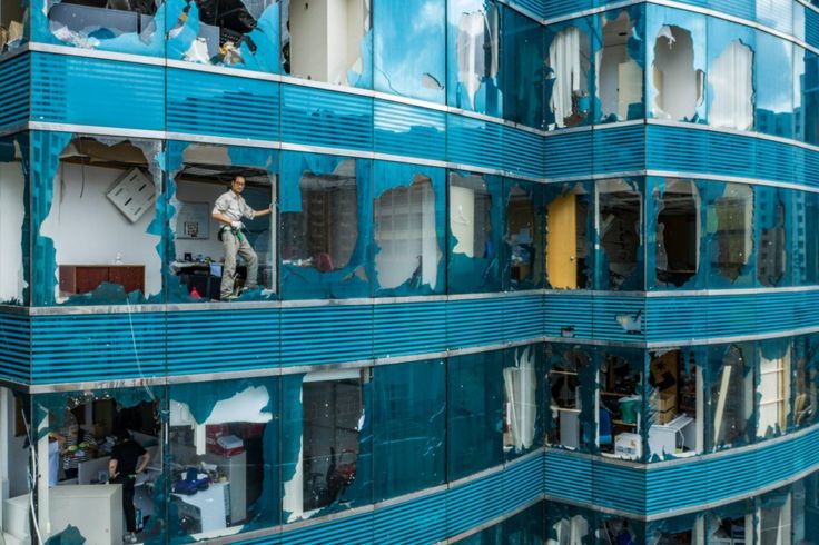 A man stands at the broken window of a building badly damaged by a typhoon