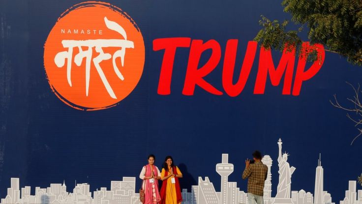 People pose for a picture in front of a hoarding of the Namaste Trump