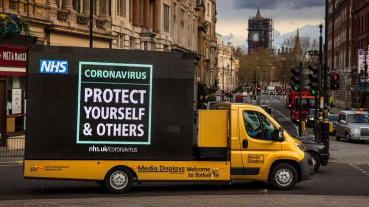 NHS slogan to protect yourself and others written on the side of a yellow van in London