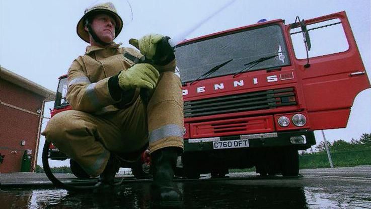 Firefighter using hose in front of fire engine