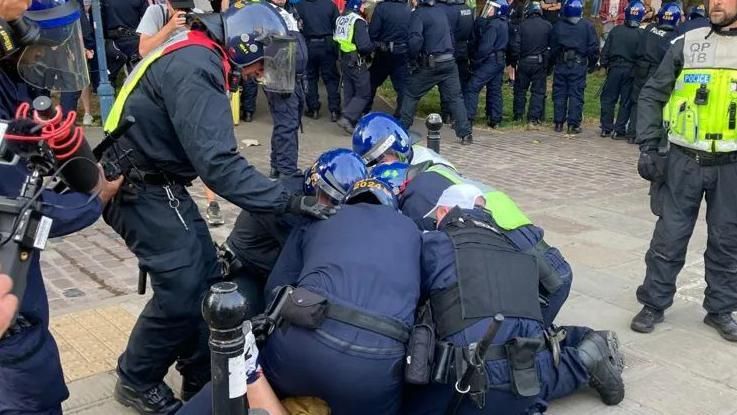 Police in Castle Park pinning one man down, with police and protesters behind.