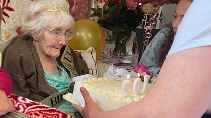 Gladys sitting in a chair having a cake presented to her
