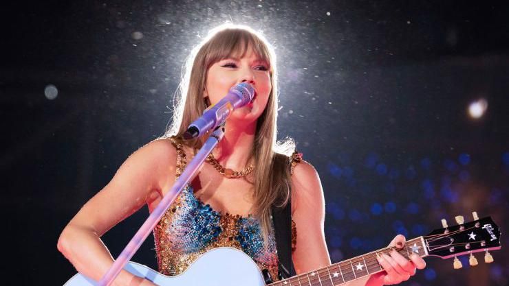 Taylor Swift singing and playing guitar in front of a microphone 