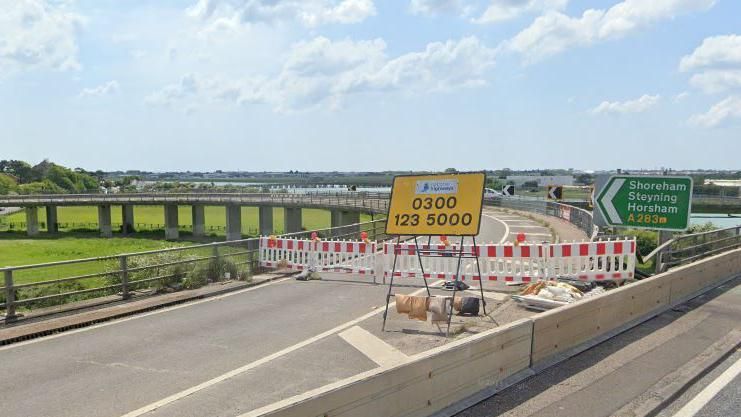 A Google Maps image of the A27 Shoreham flyover slip road with a yellow national highways sign and red and white closed barrier work across the road