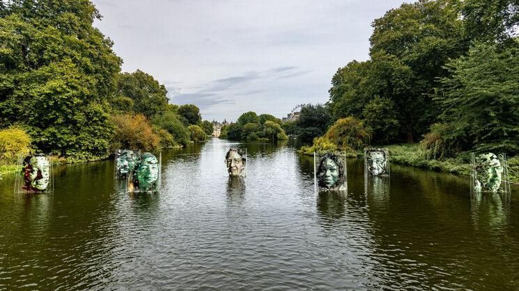 An art installation on the lake in a park. Portraits of seven huge faces on clear Perspex screens appear to float on the water.