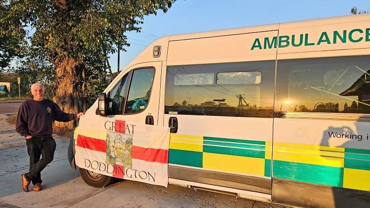 David Smith with short white hair standing next to ambulance with Great Doddington banner