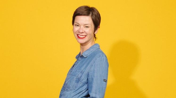 Laura Brewis smiling against a yellow background.