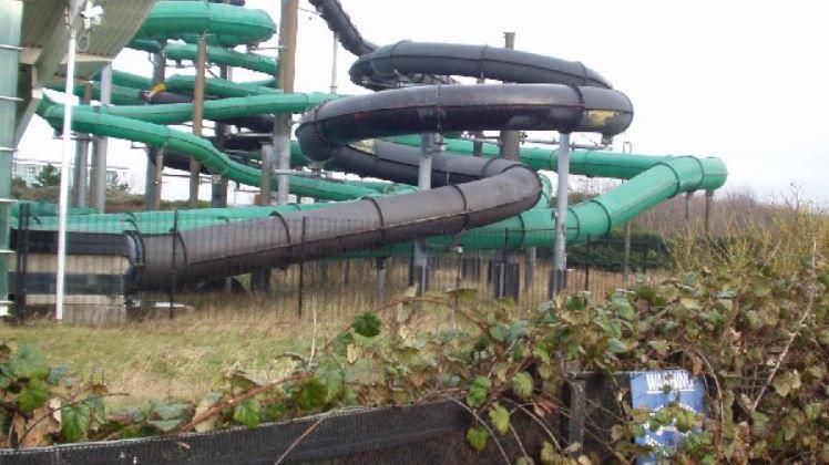 The outside of the waterpark with green and black tube slides next to a fence covered in bramble