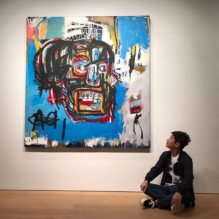 Yusaku Maezawa sitting cross-legged next to the Basquiat painting