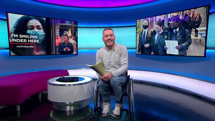 Martin on the Newsround set with pictures of people in the screen