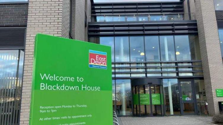 East Devon District Council headquarters showing a green sign and a brick building with large windows