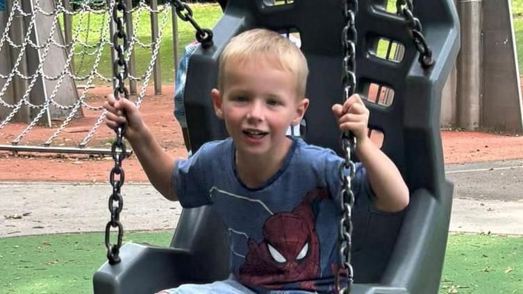 Lyle, now aged five, sits on a swing