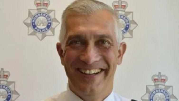 Paul Anderson smiling to the camera with logos of Humberside Police in the background on a board