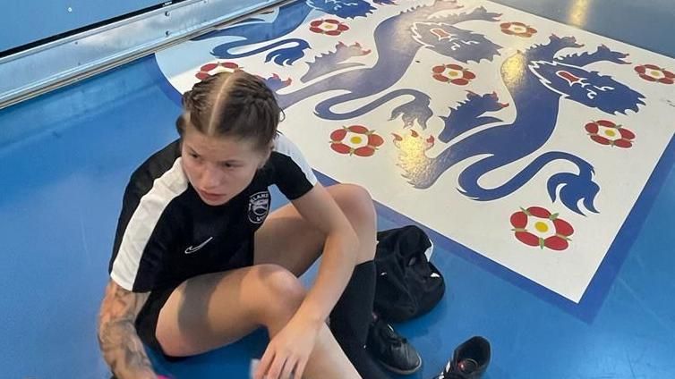 Elise Packwood sitting on a floor which has an England football badge painted on it.