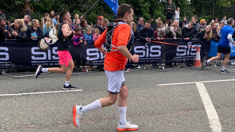 Rob running in an orange top and shorts with a roadside crowd watching