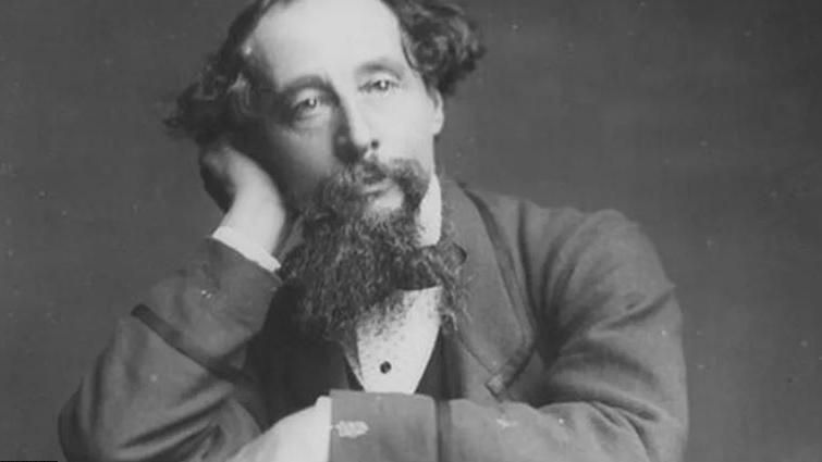 Black and white picture of Charles Dickens - a man with a long beard and long hair at the sides - resting his head in one head. 